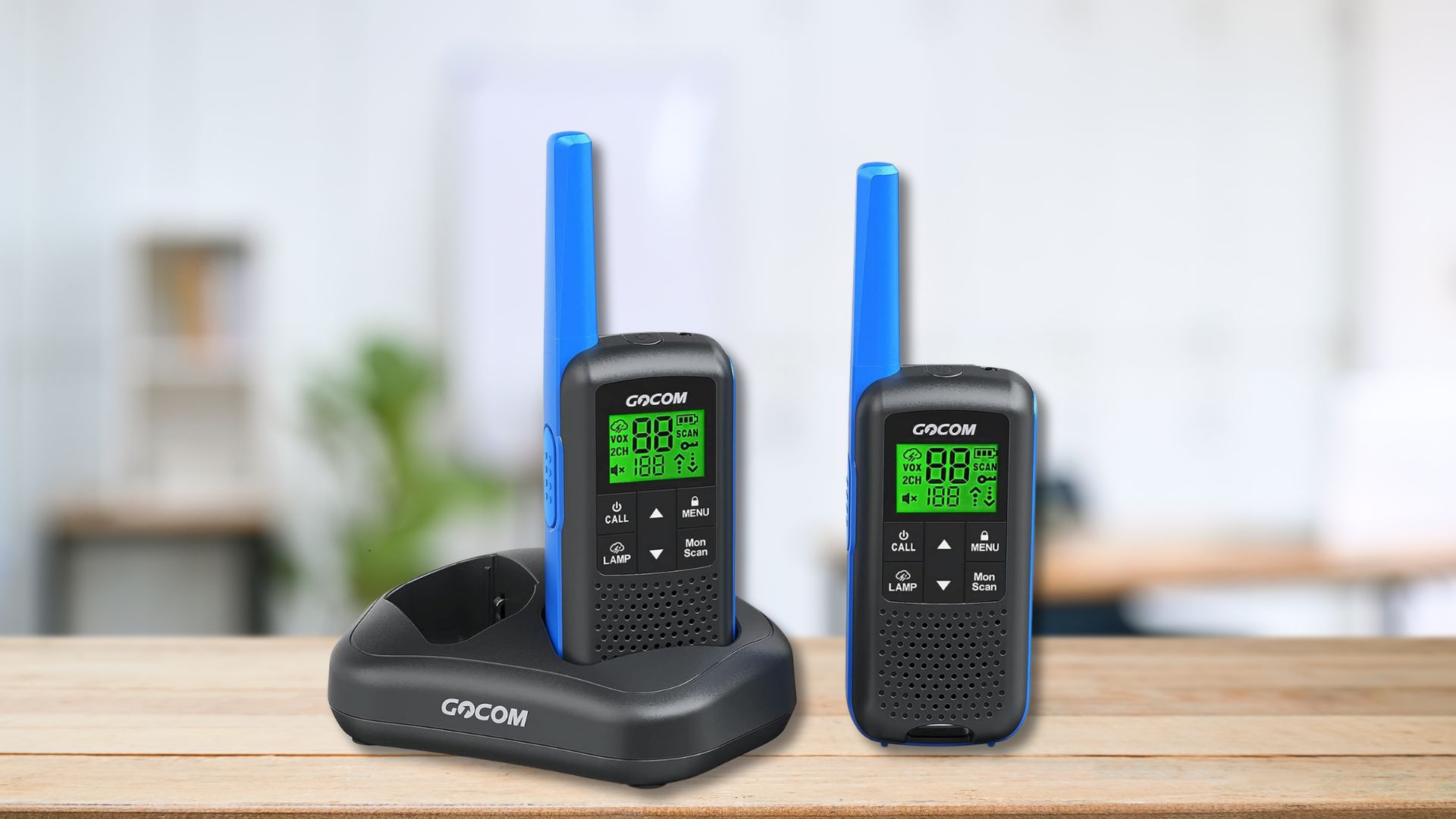 2 GOCOM FRS two way radios one sitting in a charging cradle and both sitting on a wood counter