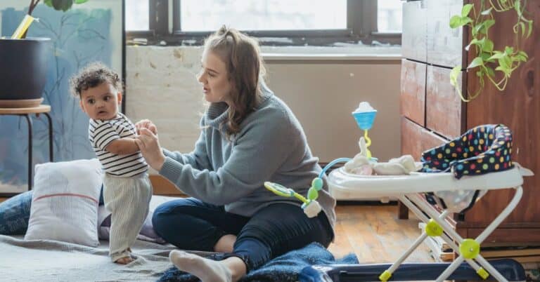 mother holding standing baby with walker in the foreground