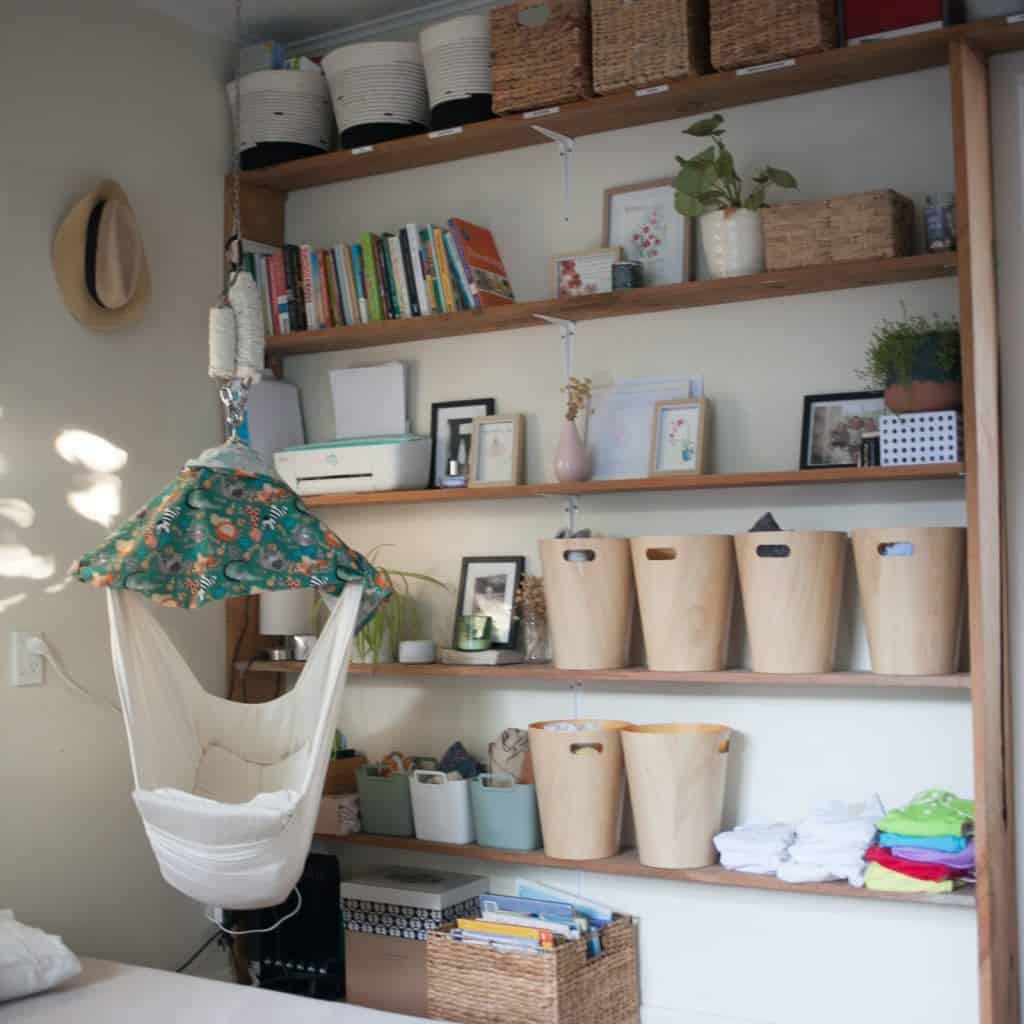A compact baby nursery corner features a hanging hammock swing and a multi-tiered shelving unit for minimalist storage
