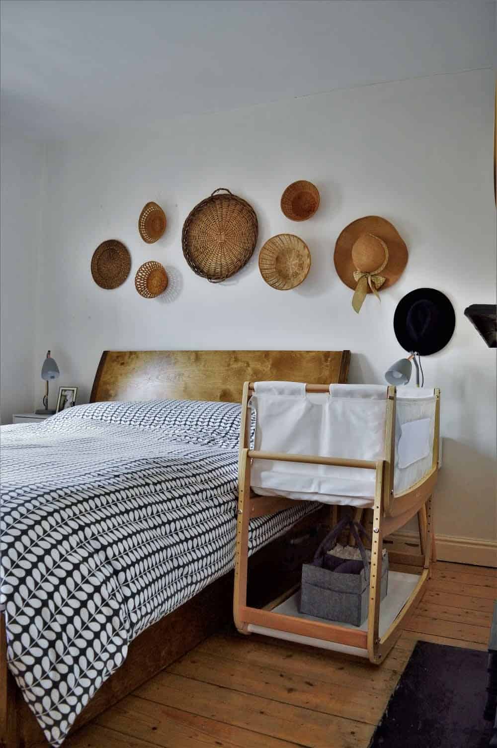 A minimalist master bedroom features a wooden bed with a black and white duvet, and a coordinated wooden baby bassinet creating a compact baby corner