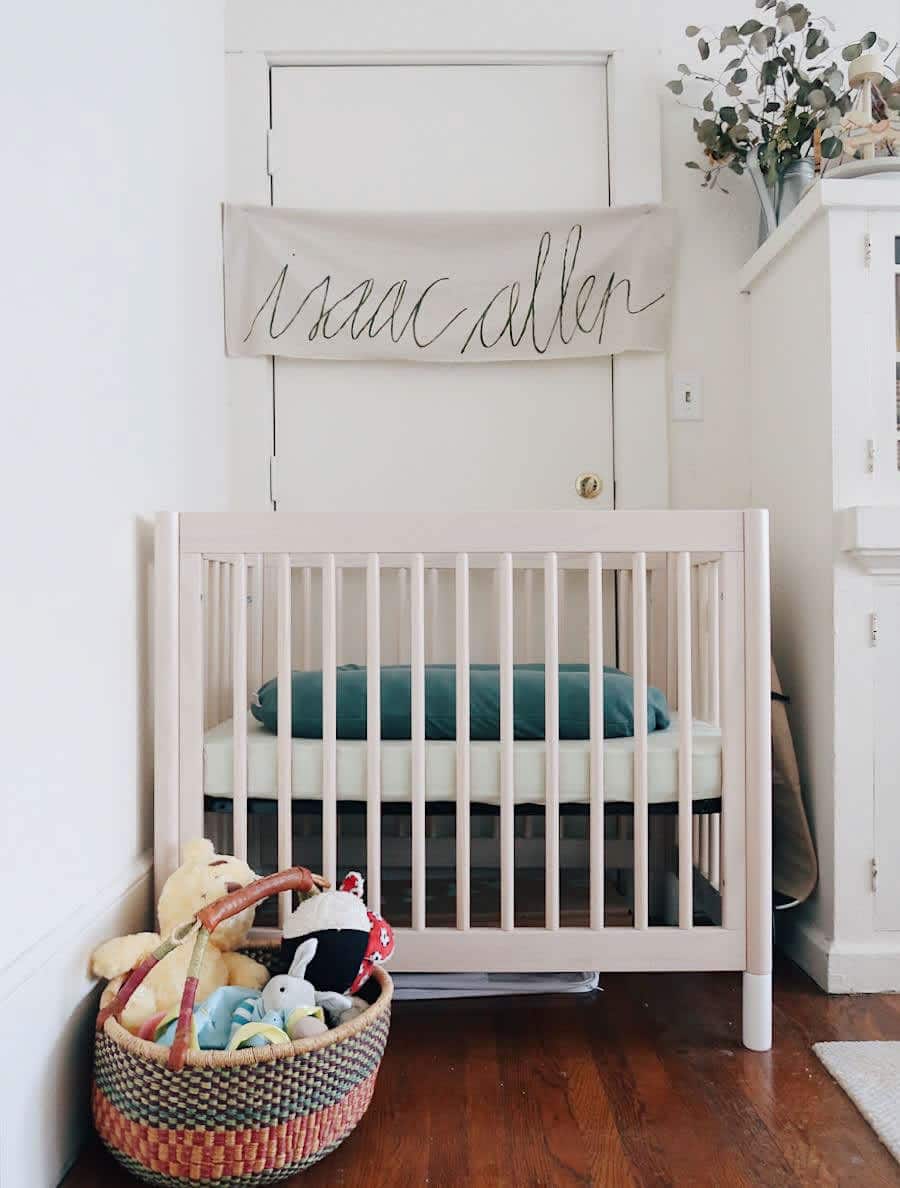 A minimalist and compact baby nursery nook with a wooden crib and name banner