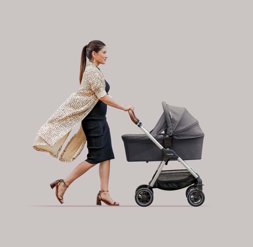 A woman pushes a gray Nuna bassinet stroller, highlighting the product's design and use nunababy